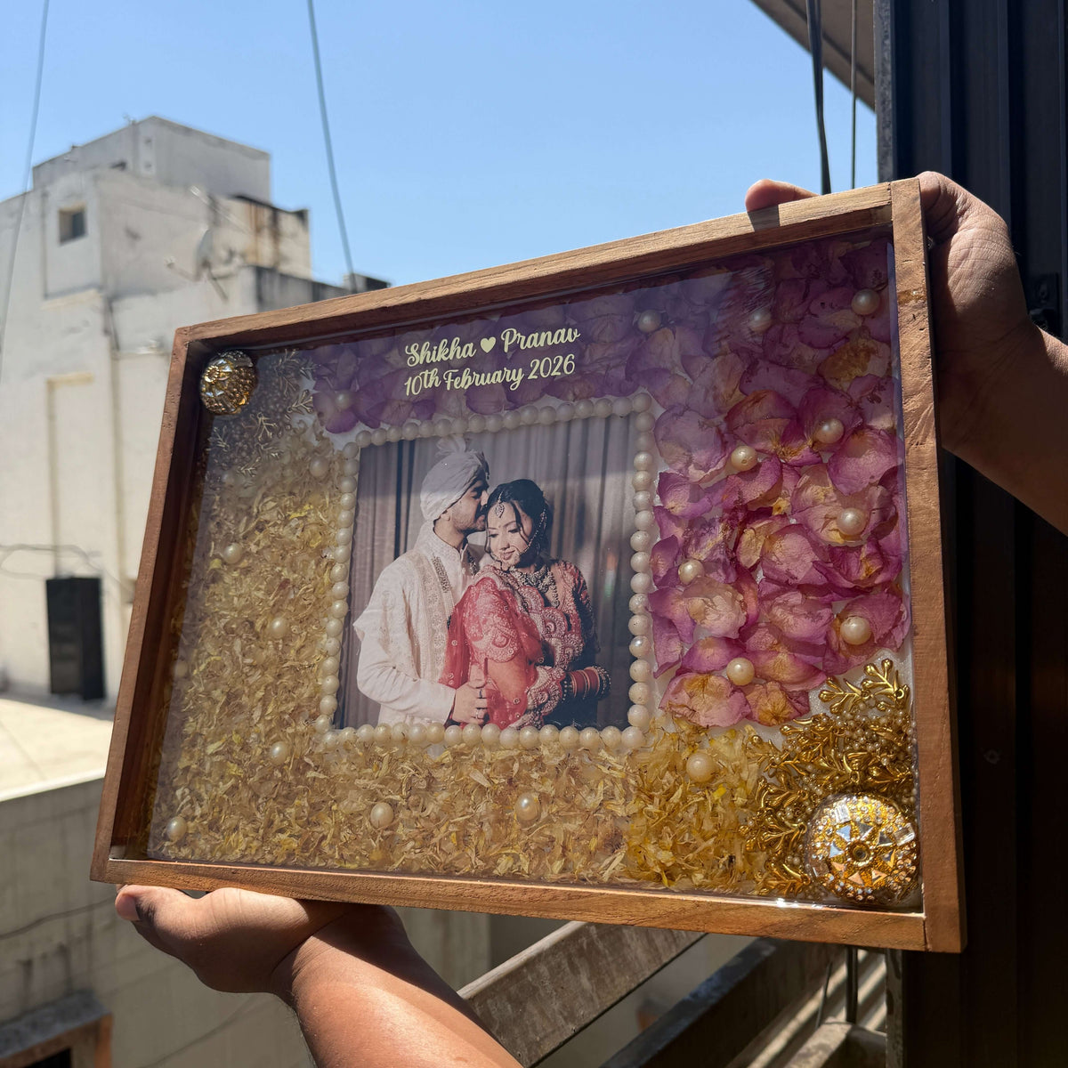 Decorative framed picture with decorative elements held by a person outdoors.